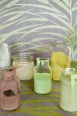Various paints in glass jars on length of yellow patterned wallpaper