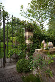 Low brick wall and open, wrought iron garden gate in mature, idyllic garden