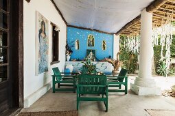 Wooden furniture on roofed terrace of Brazilian beach house with enormous supporting column; pictures of sea goddess Lemanja and altar wall in background