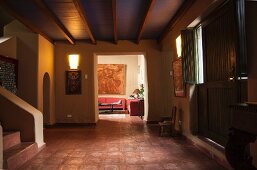 Large, dark foyer with terracotta tiles, wood-beamed ceiling and view into living room
