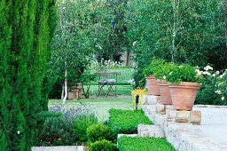 Blick in den sommerlichen grünen Park über gemauerte Terrasse mit großen bepflanzten Tontöpfen