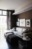 Elegant, masculine living room with pale leather couch, framed pictures on dark, structured wallpaper and glass wall
