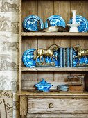 Small, brass horses in front of blue and white plates on shelves of rustic wooden dresser