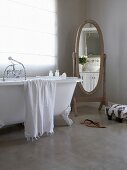 Old-fashioned free-standing mirror and claw foot bathtub standing on polished concrete floor