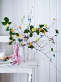 Hand-crocheted Easter bunny in front of bouquet of twigs decorated with colourful paper flowers