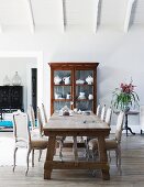 Dining area with antique, French, upholstered chairs and rustic dining table in front of white china in display cabinet