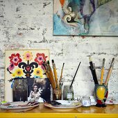 Painting utensils on console table and pictures leaning against and hung on wall