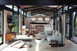 Offener Wohnraum in einem zeitgenössischem Haus - Loungebereich mit Bauhaus Schaukelstuhl und hellem Polstersofa vor Essplatz mit offener Küche
