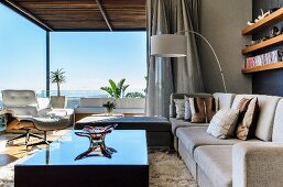Modernes Wohnzimmer mit spiegelndem Couchtisch und einer Schüssel aus Muranoglas; im Hintergrund ein weisser Eames Stuhl und der Blick bis zum Horizont