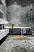 Luxurious bathroom with grey marble tiling and wooden duckboard bath mat in front of bathtub