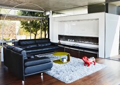 Two black leather sofas in modern living room with chrome arc lamp and open fireplace; garden terrace with pergola in background