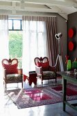 Two armchairs with red and white, polka dotted scatter cushions in front of glass wall and Oriental rug on polished concrete floor