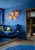 Blue lounge with velvet sofa and green scatter cushions; French club atmosphere provided by gilt, 70s chandelier with floral motif