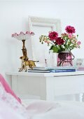 Bouquet of pink roses, antique bedside lamp and dog figurine on white-painted bedside table