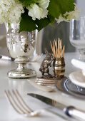 Ornamental, silver toothpick holder with hare figurine next to bouquet of white garden flowers in silver-plated vase on table