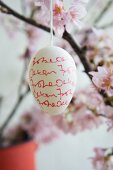 Easter egg decorated with handwriting hanging from blossoming cherry branch
