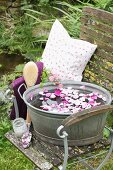 Water and rose petals in zinc tub on chair with scoop of rose bath salts