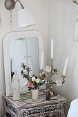 Madonnenfigur, verzierter Kerzenständer im Shabby-Stil und Frühlingsblumenstrauss vor Spiegelhintergrund auf Antiktischchen im Used-Look