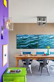 Artworks on purple wall above green drawer unit and dining area with long wooden table in front of photo art on mud-brown wall