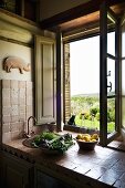 Bowls of lemons and vegetables on tiled sink unit in Tuscan, vintage kitchen; wide view through open window