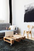 Wooden palette used as coffee table in front of sofa and black and white textile artwork on wall