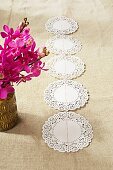 Row of doilies on linen fabric next to pink potted orchid