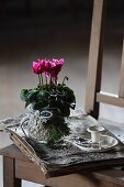 Pink cyclamen, Christmas decorations, birch bark and vintage candlestick on bundle of paper loosely bound in birch bark