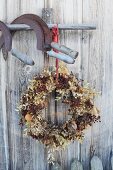 Autumnal wreath with berries under rusty sickles hanging from wooden pole