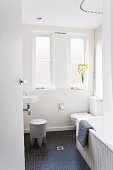 Kunststoff-Hocker vor Waschbecken, Toilette und Badewanne im Bad mit schwarzen Mosaik-Bodenfliesen