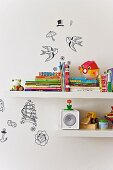Ausschnitt von weissen Wandbords mit Kinderbüchern und Spielzeug, verschiedene Deko-Applikationen an Wand