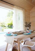 Holzverkleidetes Esszimmer mit Blick auf Pool - Heller Holztisch mit rustikaler Holzschale und weiße Kunststoff Schalenstühle