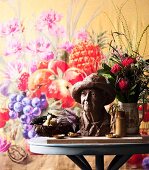 Small bust and bouquet on round table in front of floral wall hanging