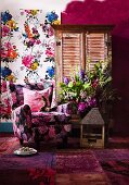 Floral sofa, old birdcage, patchwork rug in various shades of red, bouquet, cupboard with louver doors and floral wall hanging