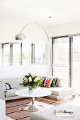 Corner sofa, arc lamp and round coffee table in front of glass doors with louver blinds