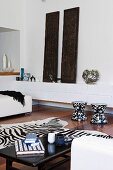 White lowboard with vases and carved, Indian wooden panels, in front of it black and white stools, zebra fur and coffee table in a bright living room