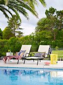 Two sun loungers with patterned cushions by the pool in front of glass balustrades and garden views