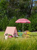 Tent-shaped wooden frame covered with patterned fabric next to colorful garden chairs and a red and white parasol