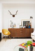Fifties-style, engineered-wood shell chairs, pictures and coloured bottles on top of 70s sideboard and stag's antlers on wall