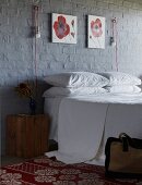 Doppelbett an grau gestrichener Ziegelwand mit rot-weißen Blumenbildern und innovativen Wandleuchten