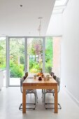 Designer Holztisch mit verschiedenen Stühlen vor Glasfront zum sommerlichen Garten in restauriertem Altbau mit Oberlicht