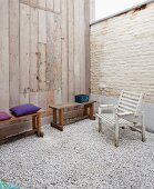 Courtyard with gravel floor, fold-down wooden table in wall panelling, wooden benches and wooden chair