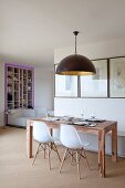 Open-plan kitchen with wooden table and white designer chairs below black pendant lamp