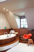 Klassiker Schaukelstuhl in Rot und Hocker aus Holz neben ovaler Badewanne mit Holzverkleidung und umlaufender Stufe im Dachzimmer mit Gaubenfenster