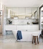 Spacious, bright gray and white bathroom with free standing bathtub and mirrored floating cabinets