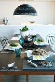 Stylishly set table with oysters on white, designer china plates and blue drinking glasses