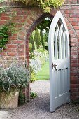 White, wooden, Gothic-style open garden gate in brick wall with view of topiary box trees beyond