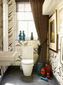 Grossformatige Fliesen mit floralem Muster in Bad mit drapiertem Fenstervorhang & Retro-Vasensammlung neben Toilette