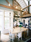 Converted industrial building with wooden gallery and white lattice windows in dining room and view into cosy, country-house-style living area