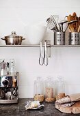 Kaffeemaschine und Aufbewahrungsgläser, davor Brot und Butter auf Ablage, an weisser Holzwand montierte Wandkonsole mit Kochgeschirr, Behältern und aufgehängten Zangen