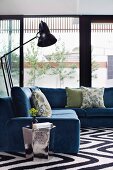 Comfortable grey-blue corner sofa, retro standard lamps and shiny side table in front of glass walls